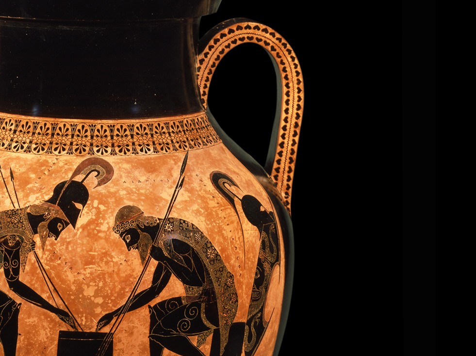 A picture of a Greek amphora, made of clay. Two heroes from the epic poem the Iliad, identified as Achilles and Ajax, are seated on a small bench, in front of a small table, playing a game of dice. Both are holding their spears in one hand and pointing to the table with the other. Achilles wears his helmet, and the shields of both heroes lie behind them. From the mouth of Achilles, a Greek word meaning “four” is spelled out. From the mouth of Ajax, the word spelled out means “three”.